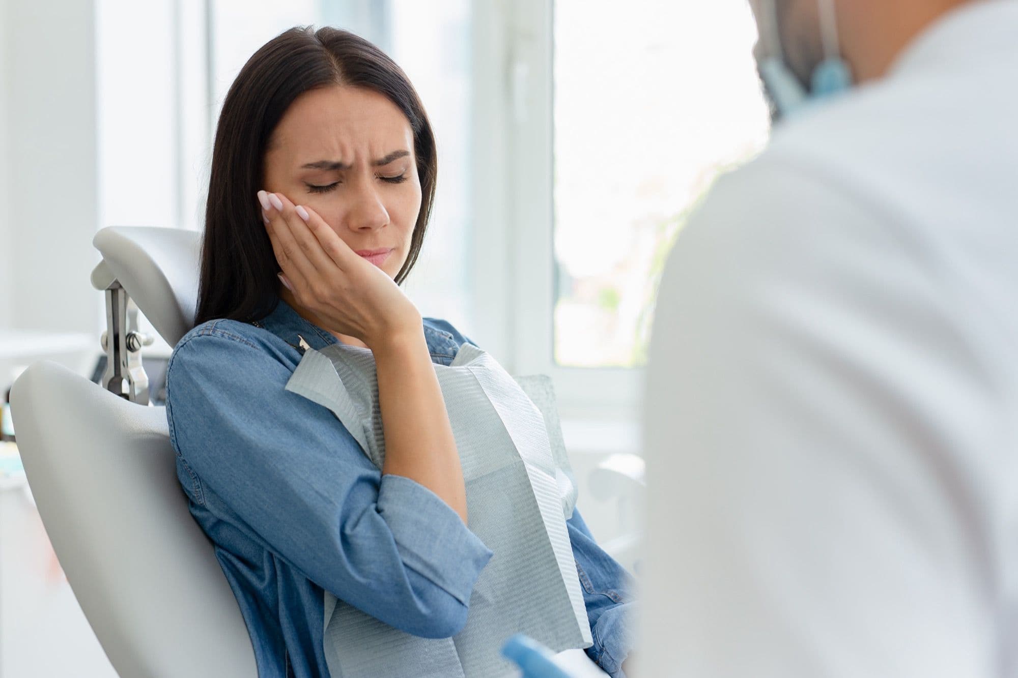 Paciente en sillón dental sosteniéndose la mejilla con gesto de dolor