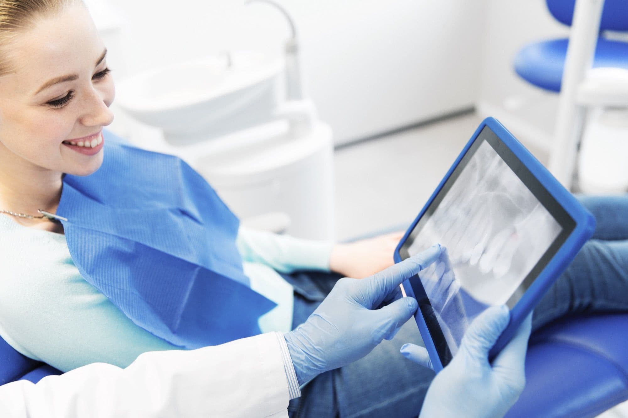 Paciente sonriendo mientras el dentista revisa una radiografía digital en tablet